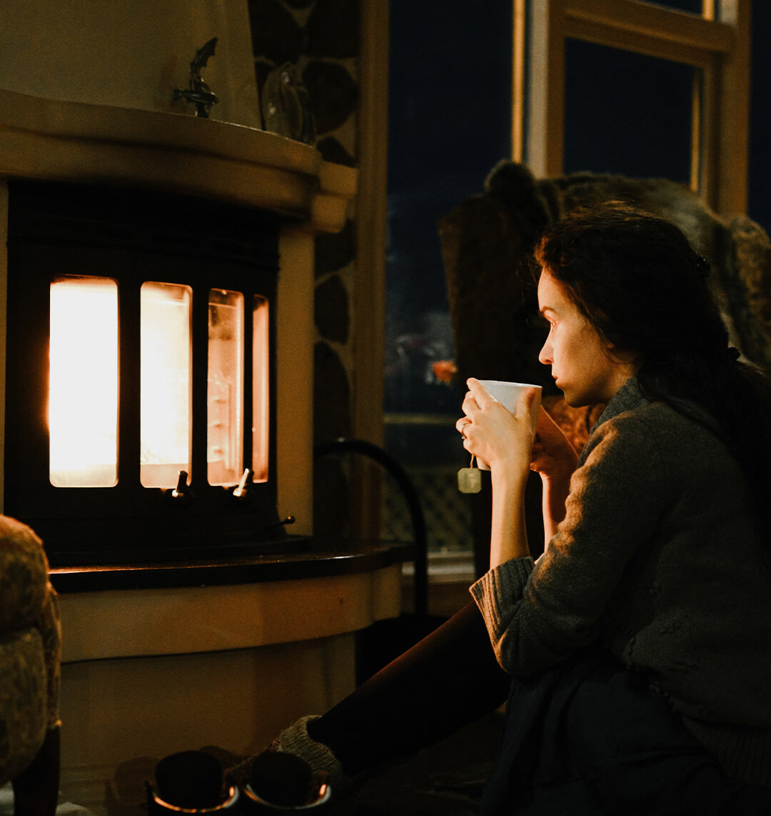 Dame som sitter foran peisen på kvelden