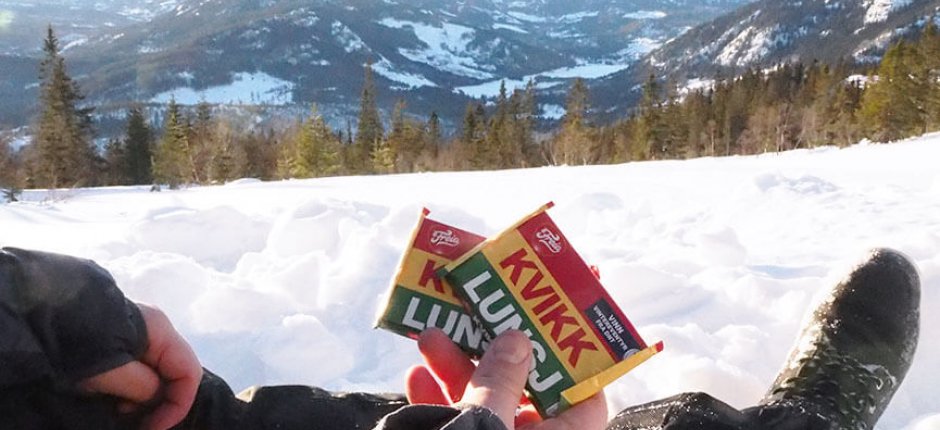 Mann med Kvikklunsj i snøen foran norsk natur