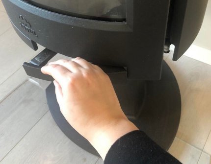 Hånd åpner døren til vedovnen forsiktig