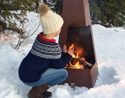 Jente sitterå varmer seg i snøen foran utepeisen Jøtul Terrazza